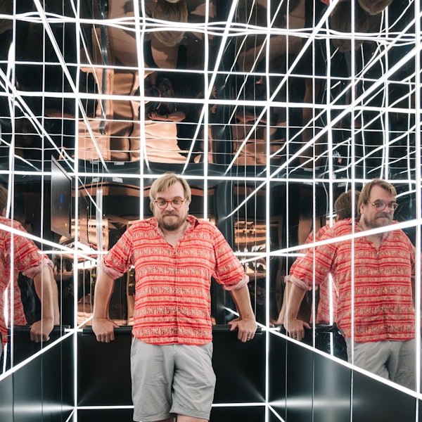 Nilz Bokelberg steht in einem verspiegelten Aufzug mit Leuchtröhren.