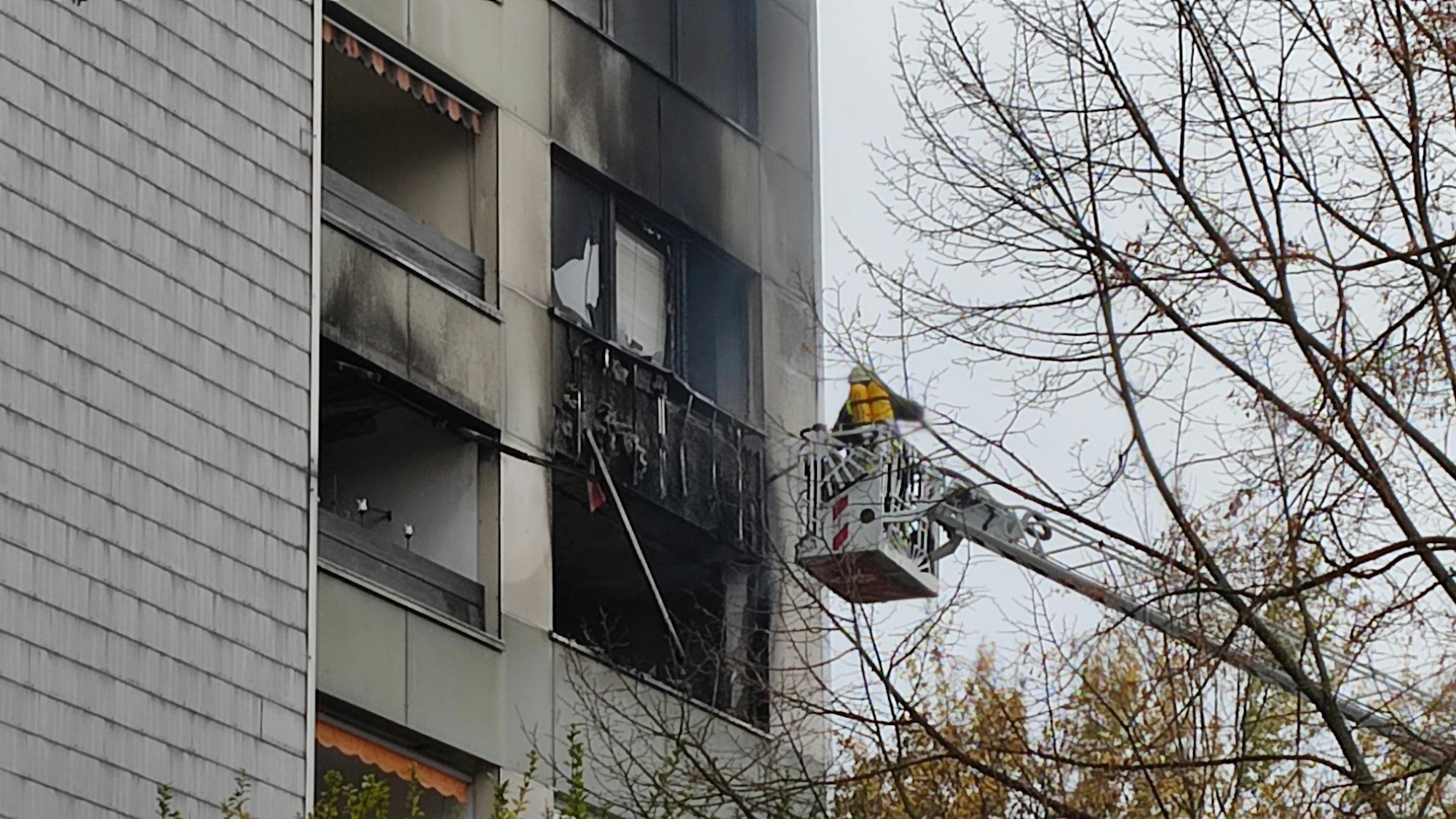 Ein Feuerwehrmann steht auf einer Drehleiter an einem Balkon eines Mehrfamilienhauses in Köln-Neubrück.
