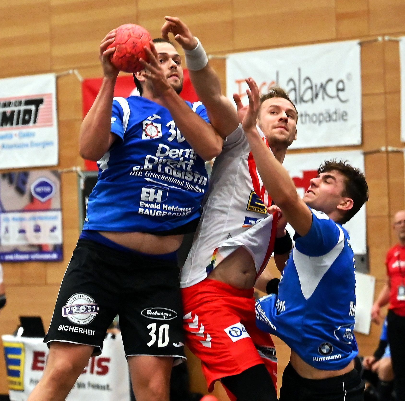 Ein Handballspieler versucht, sich zwischen zwei Gegner zu drängen und seinen Gegenspieler am Wurf zu hindern.