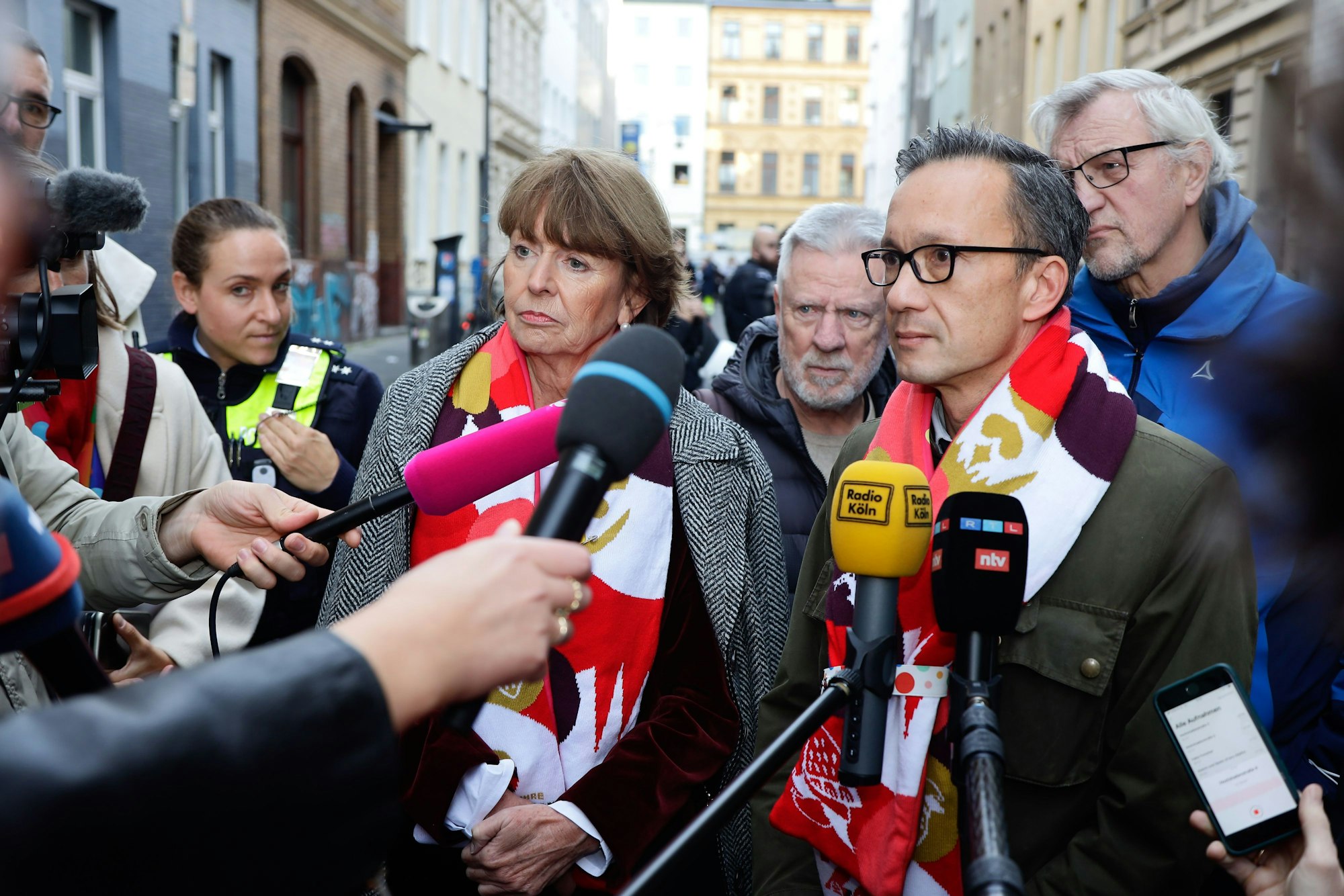 Oberbürgermeisterin Henriette Reker und Polizeipräsident Köln Falk Schnabel stehen am 11.11. auf der vollen Zülpicher Straße und sprechen in die Mikrofone von Journalisten.