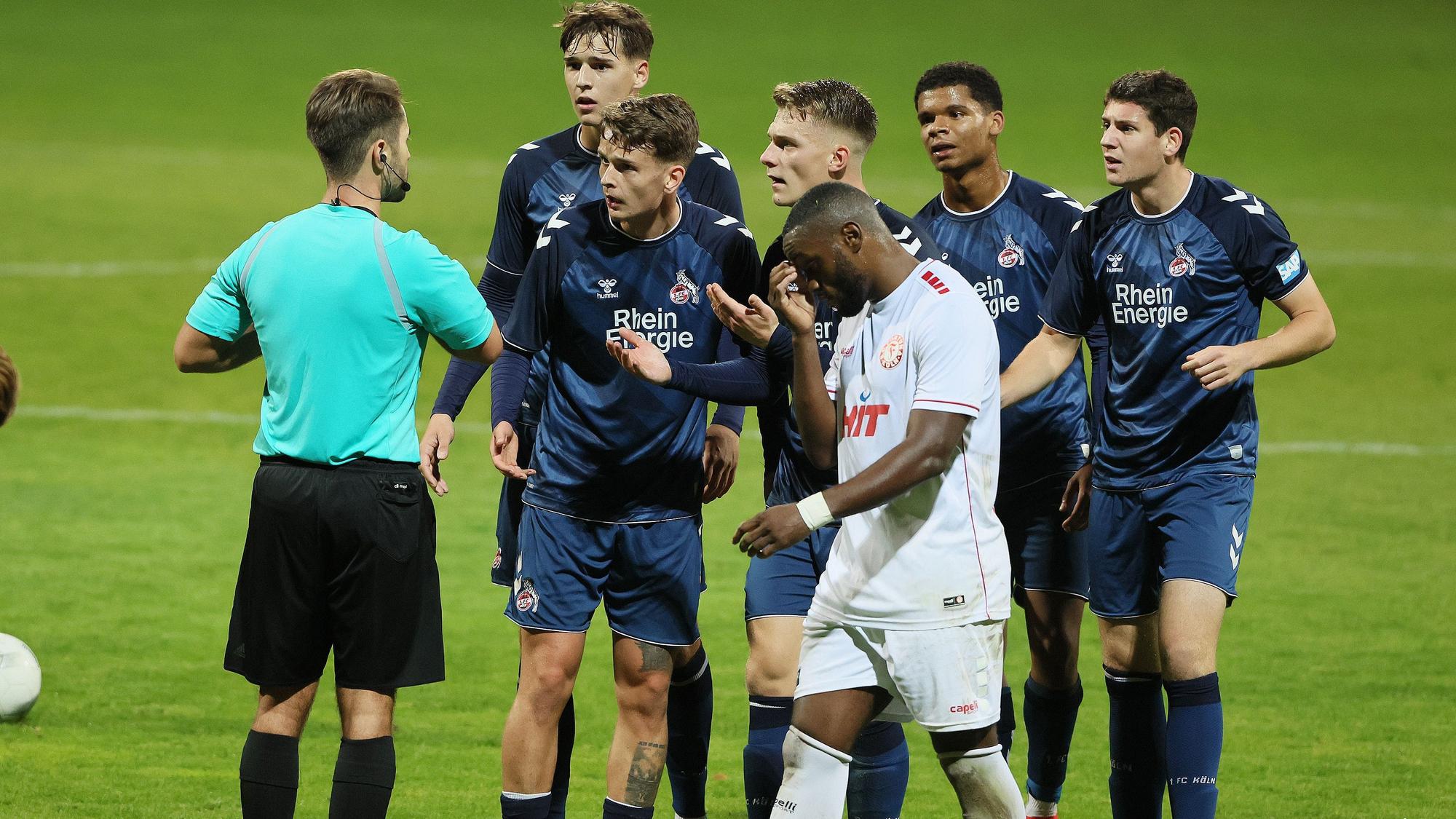 Fünf Fußballspieler stehen vor dem Schiedsrichter und reden auf ihn ein.