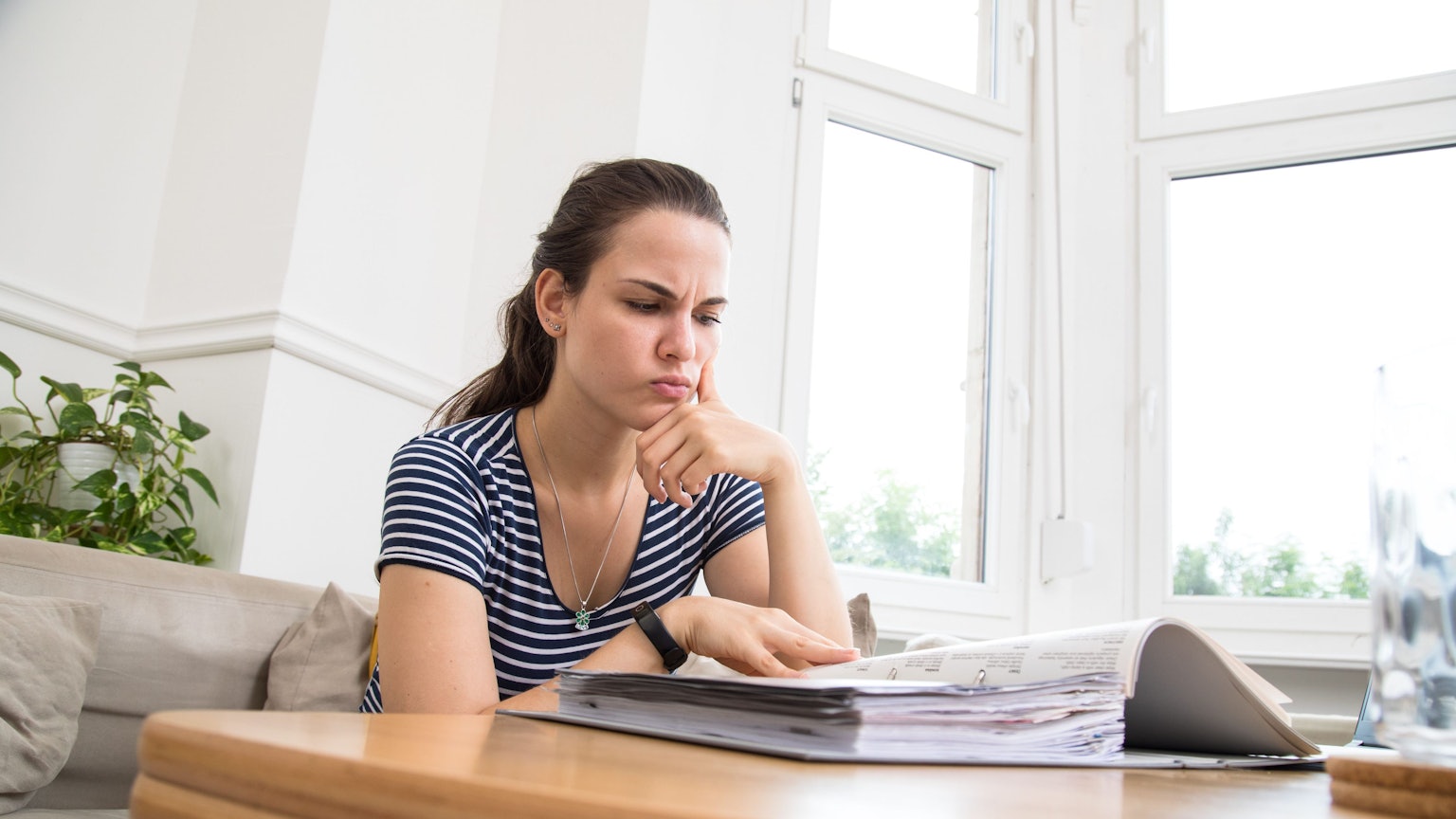 Eine Frau blickt kritisch auf einen Aktenordner mit Rechnungen.
