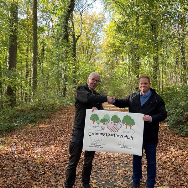 Forstamtsleiter Stephan Schütte und Uwe Zaar, Kreisdezernent Umwelt, Planung und Verkehr, halten im Königsdorfer Forst den Vertrag hoch, mit dem die Zusammenarbeit besiegelt wurde.