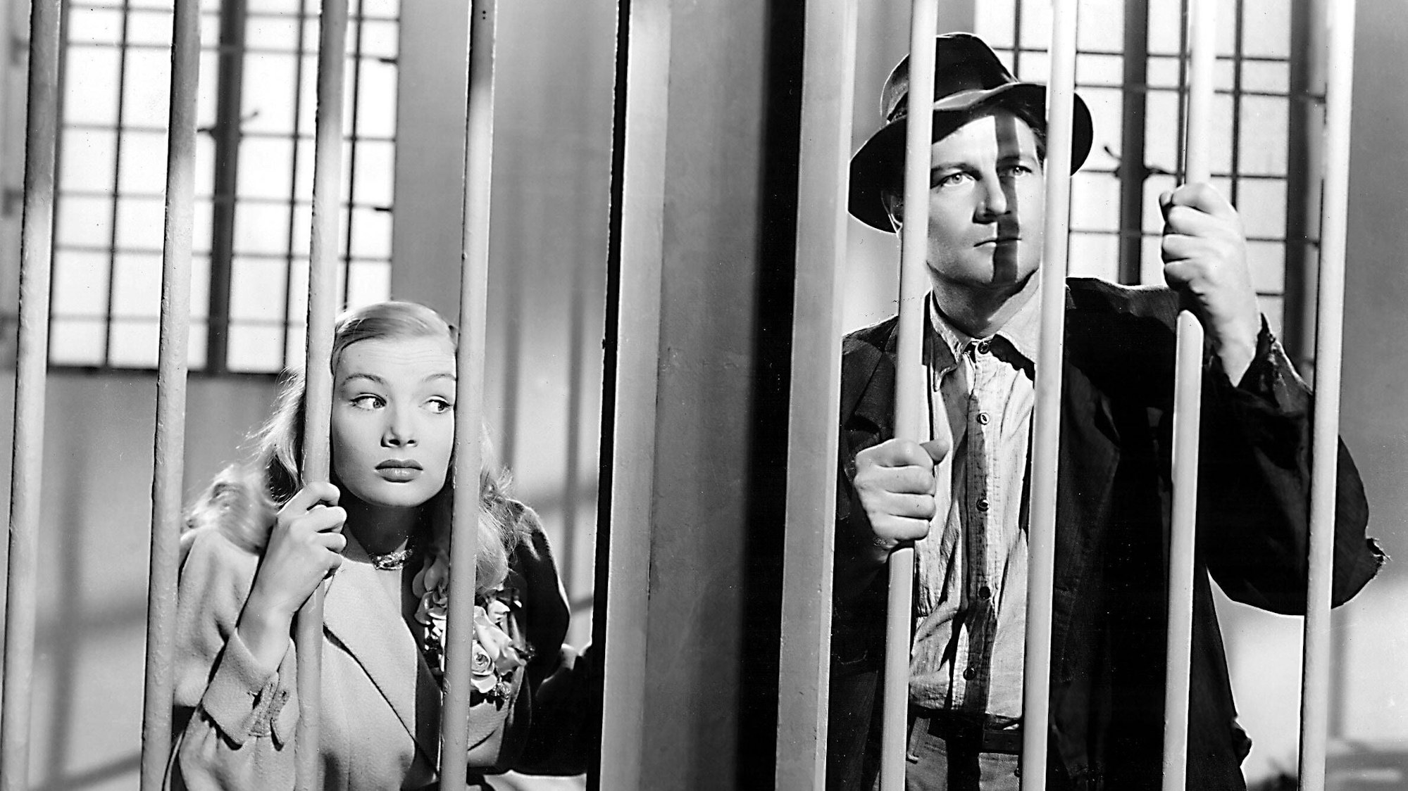 Veronica Lake und Joel McCrae hinter Gittern. Veronica Lake versucht, ihr Gesicht durch die Stäbe zu schieben.