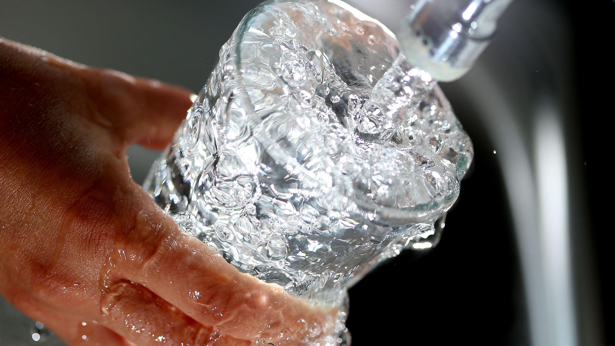 Ein Glas wird mit Wasser aus dem Hahn gefüllt und läuft über.
