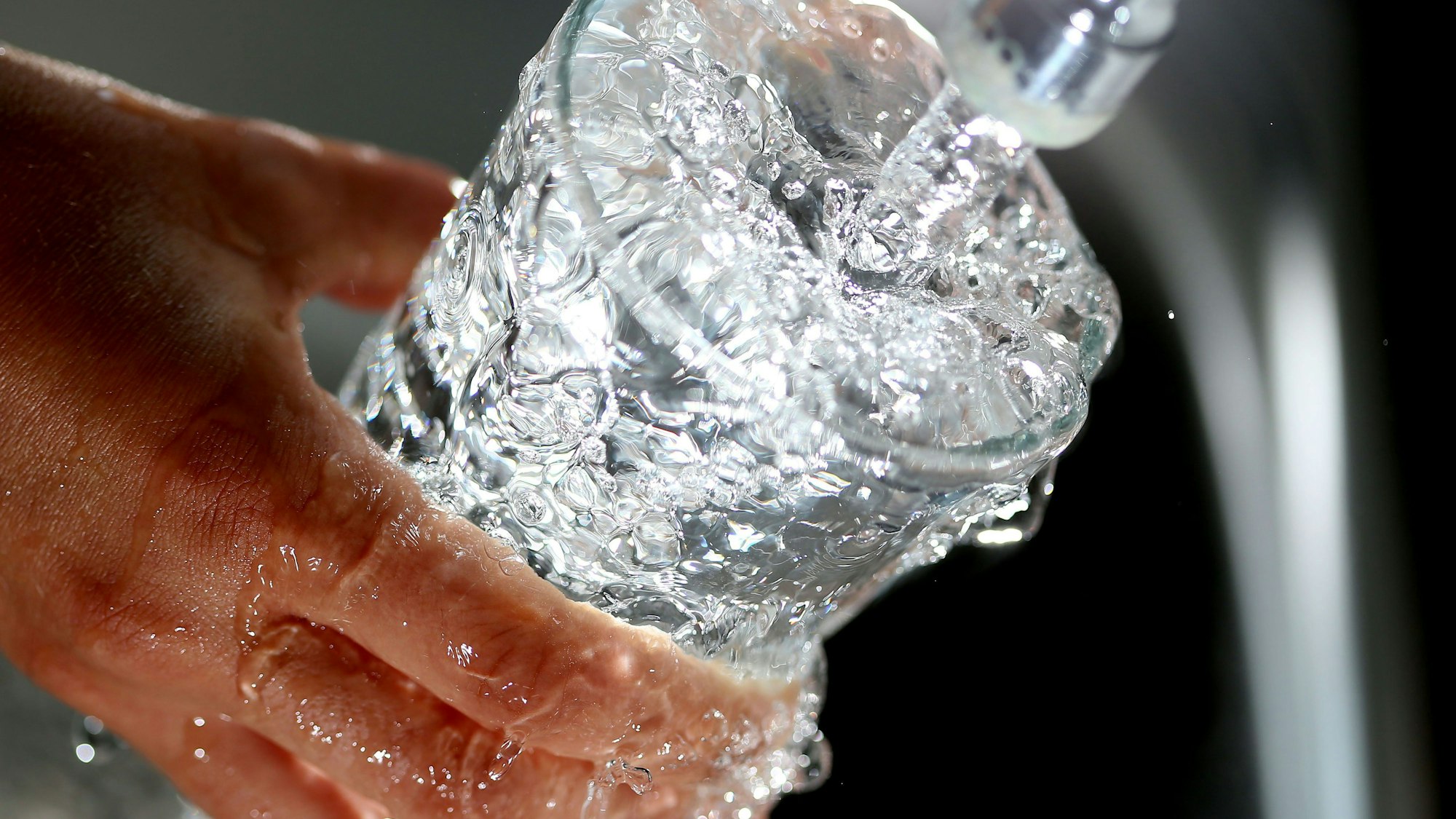 Wasser läuft unter einem Hahn in ein Glas.