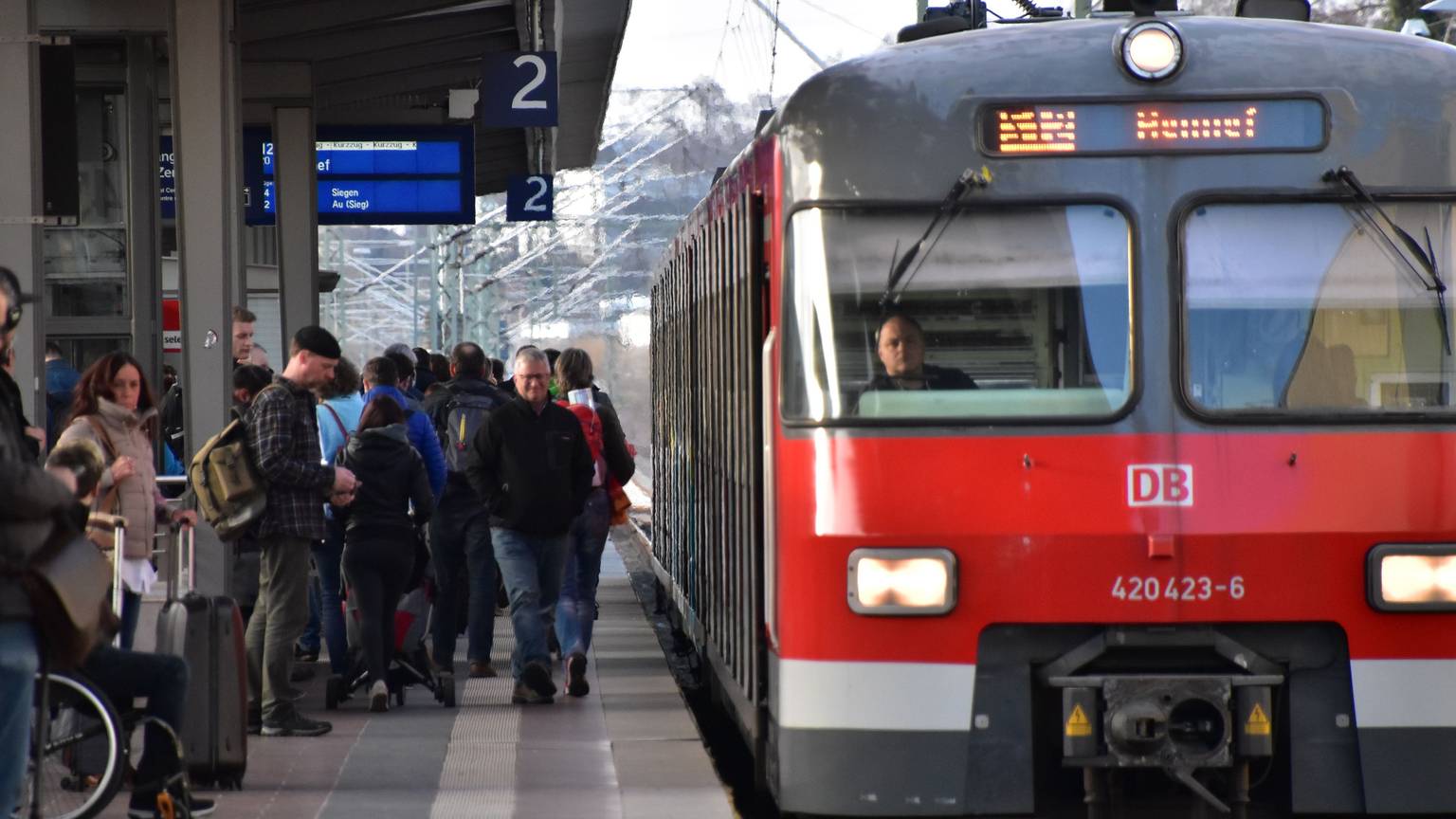 Die S12 steht an einem Bahngleis. Viele Leute warten auf dem Bahnsteig.