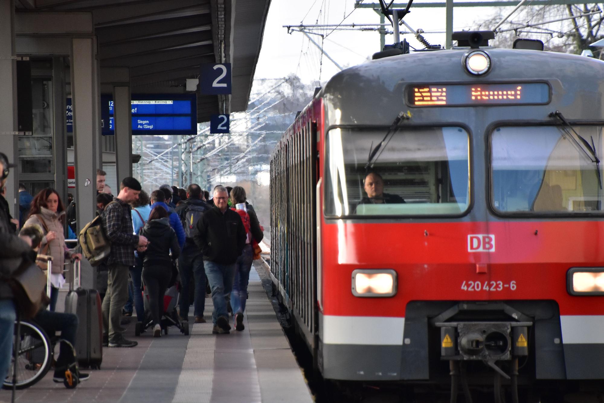 Die S12 steht an einem Bahngleis. Viele Leute warten auf dem Bahnsteig.