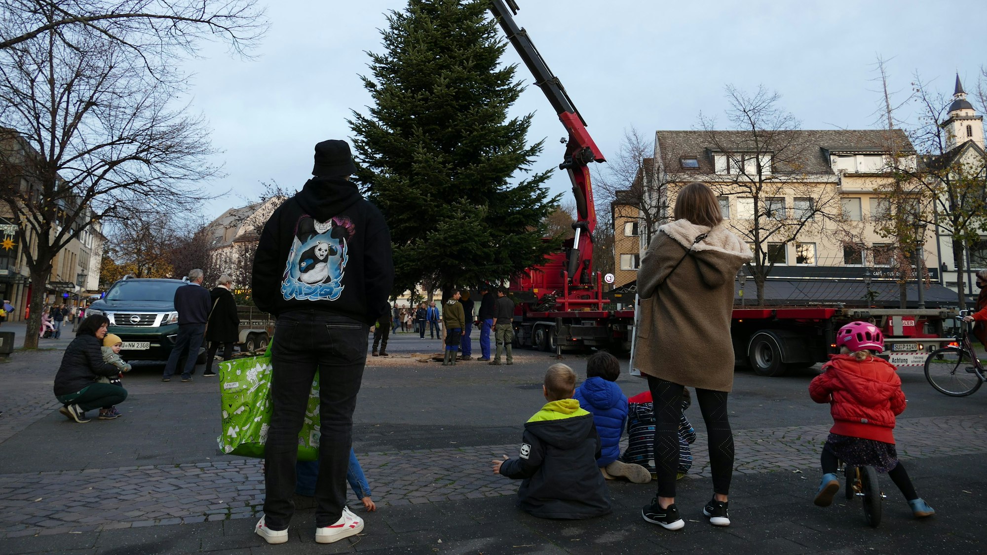 Ein Kran hat die Tanne auf dem Siegburger Markt aufgestellt. Viele Passanten mit Kindern blieben stehen und beobachten die Szene.