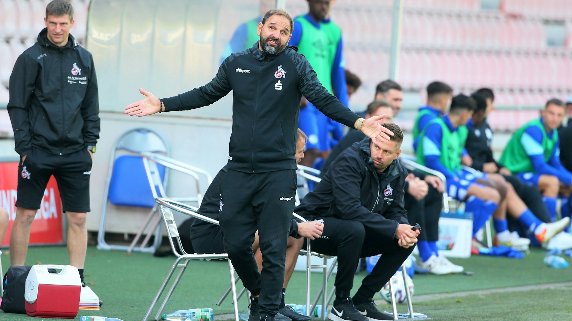 Ein Trainer steht am Spielfeldrand und breitet die Arme aus.