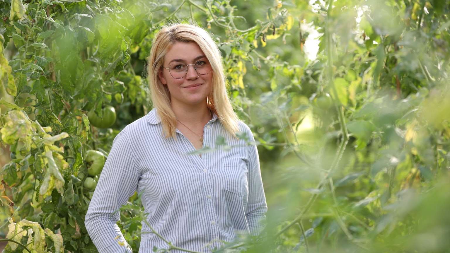 Caroline Uhl steht inmitten grüner Pflanzen.