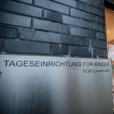 Ein Schild „Tageseinrichtung für Kinder, 51381 Leverkusen“ ist an einer Gebäudewand angebracht.