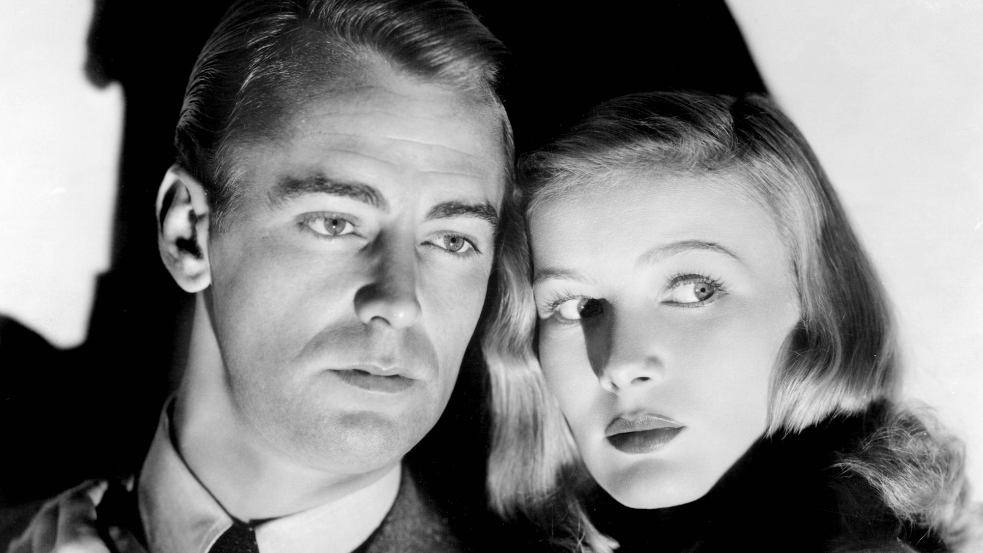Alan Ladd und Veronica Lake in Licht und Schatten. Sie schauen seitlich ins mysteriöse Licht.