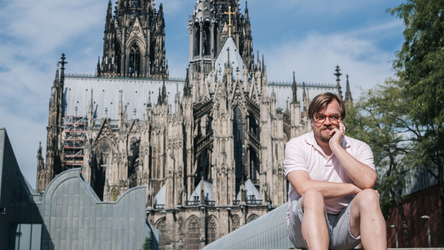 Der Moderator und Autor Nilz Bokelberg sitzt vor dem Kölner Dom.