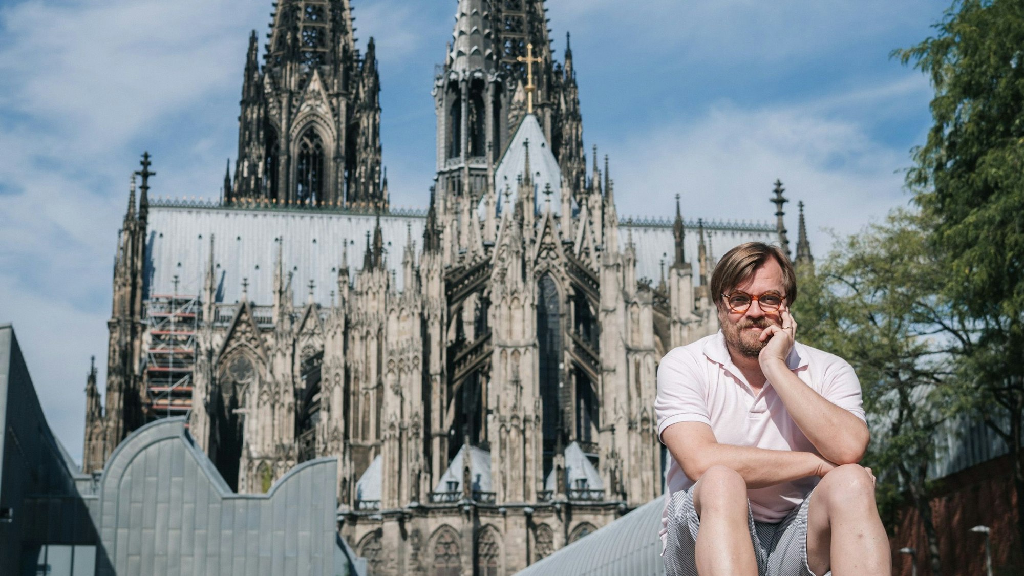 Der Moderator und Autor Nilz Bokelberg sitzt vor dem Kölner Dom.