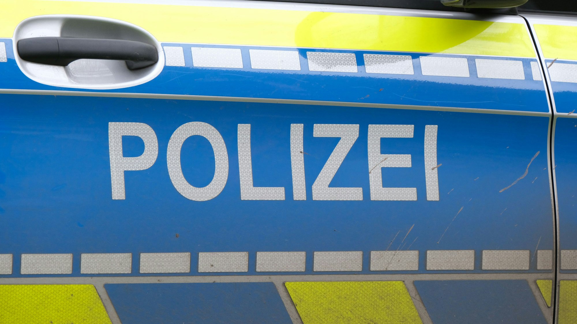 Auf der Türe eines Polizeiautos ist der Schriftzug „Polizei“ zu lesen.