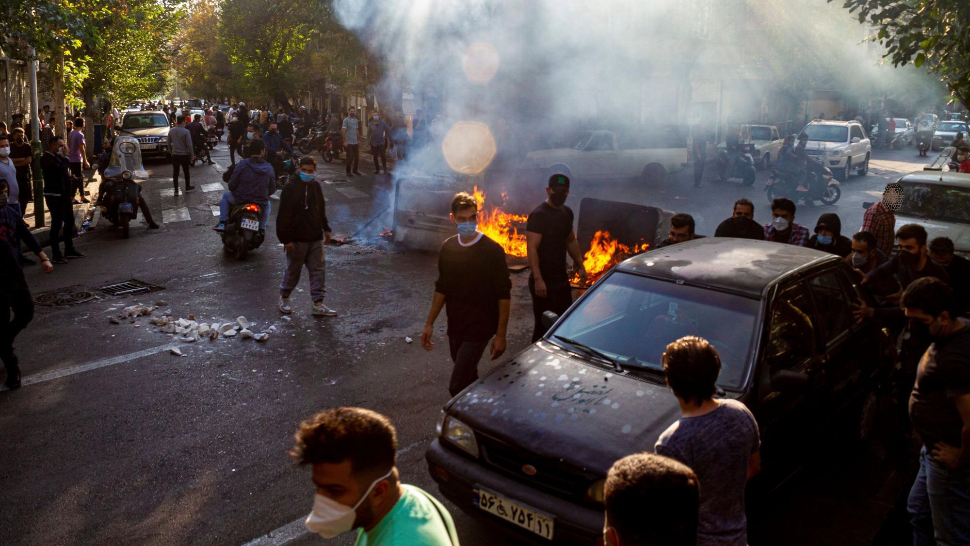 Menschen protestieren in Teheran auf der Straße und haben Barrikaden errichtet. Es brennen Feuer. Viele Demonstranten tragen Gesichtsmasken.