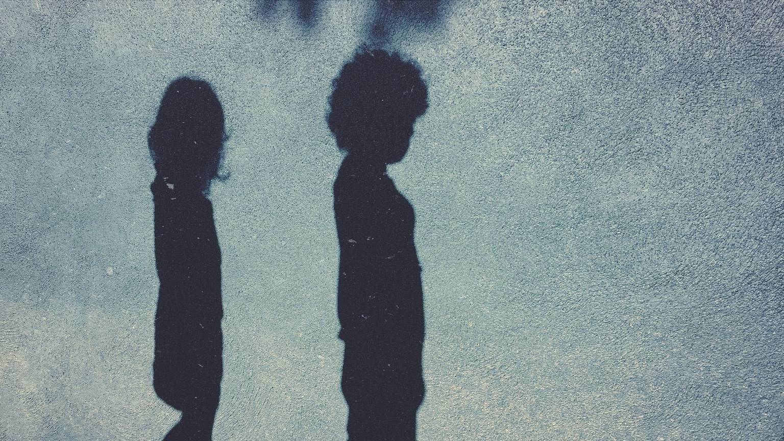 Die Schatten eines Jungend und eines Mädchens sind auf einer blauen Hauswand zu sehen.
