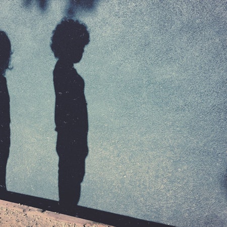 Die Schatten eines Jungend und eines Mädchens sind auf einer blauen Hauswand zu sehen.