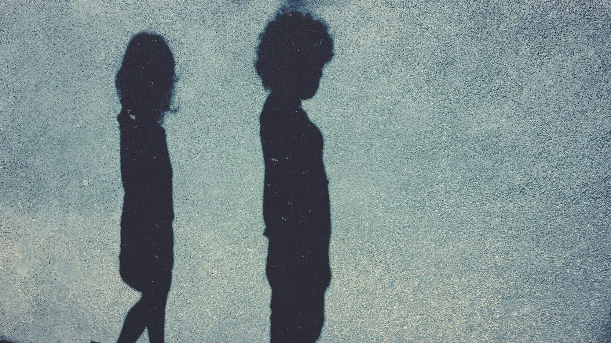 Vor einer blauen Wand sieht man den Schatten eines Jungen und eines Mädchens.