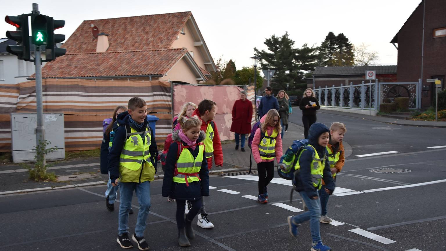 Schulkinder in gelben Warnwesten überqueren die Straße an einer Ampel.