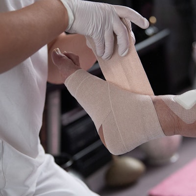 Eine Pflegefachkraft legt einen Kompressionsverband an einem Fuß an.