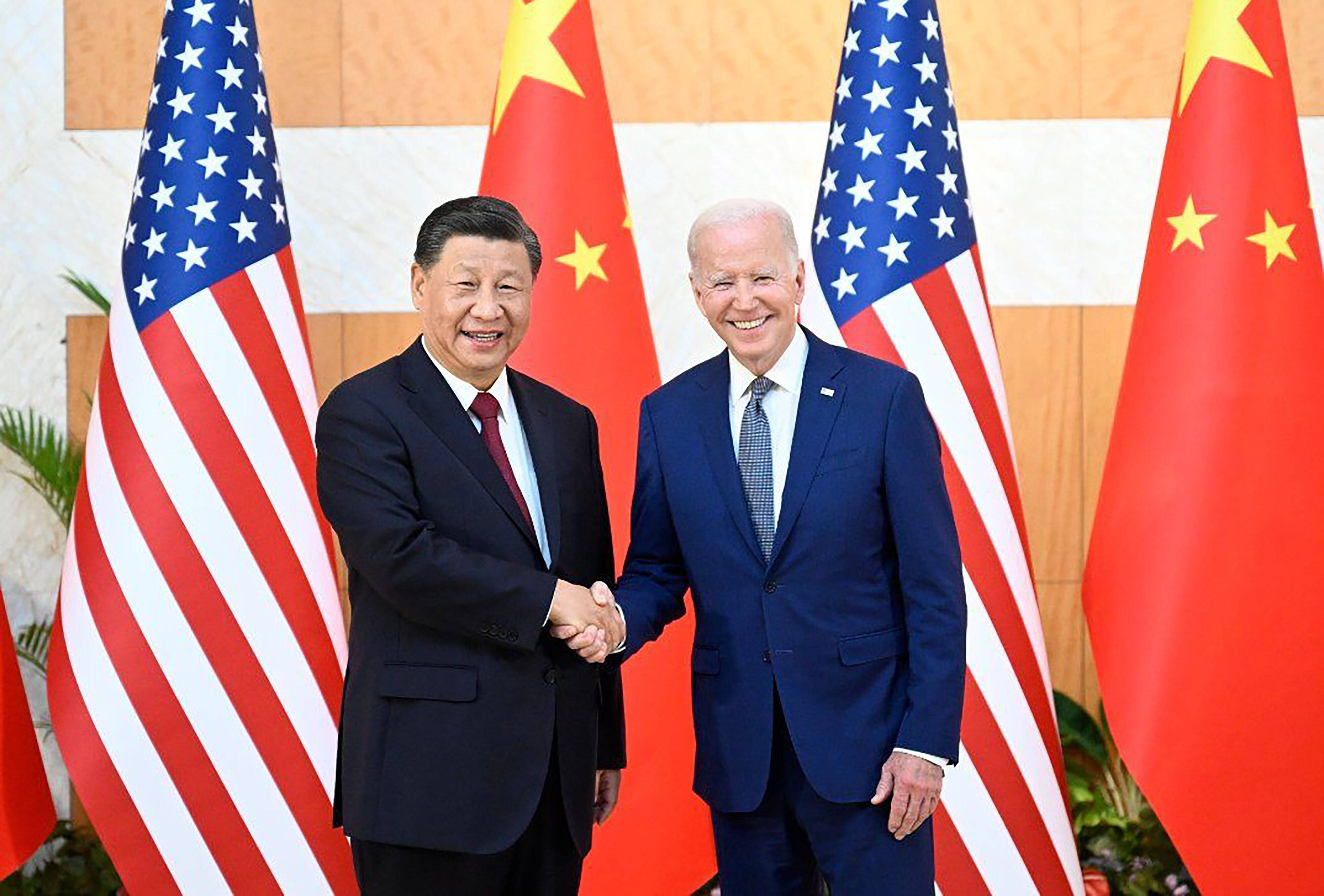 US-Präsident Joe Biden (r) und Chinas Präsident Xi Jinping (l) schütteln grinsend Hände, während sie sich im Rahmen des G20-Gipfels in Bali treffen. Im Hintergrund die Flaggen von China und der USA.