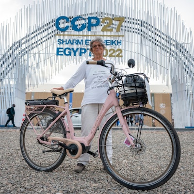 Es ist Frau Hildebrandt mit ihrem Fahrrad zu sehen, wie sie vor dem Eingang des UN-Klimagipfels steht.