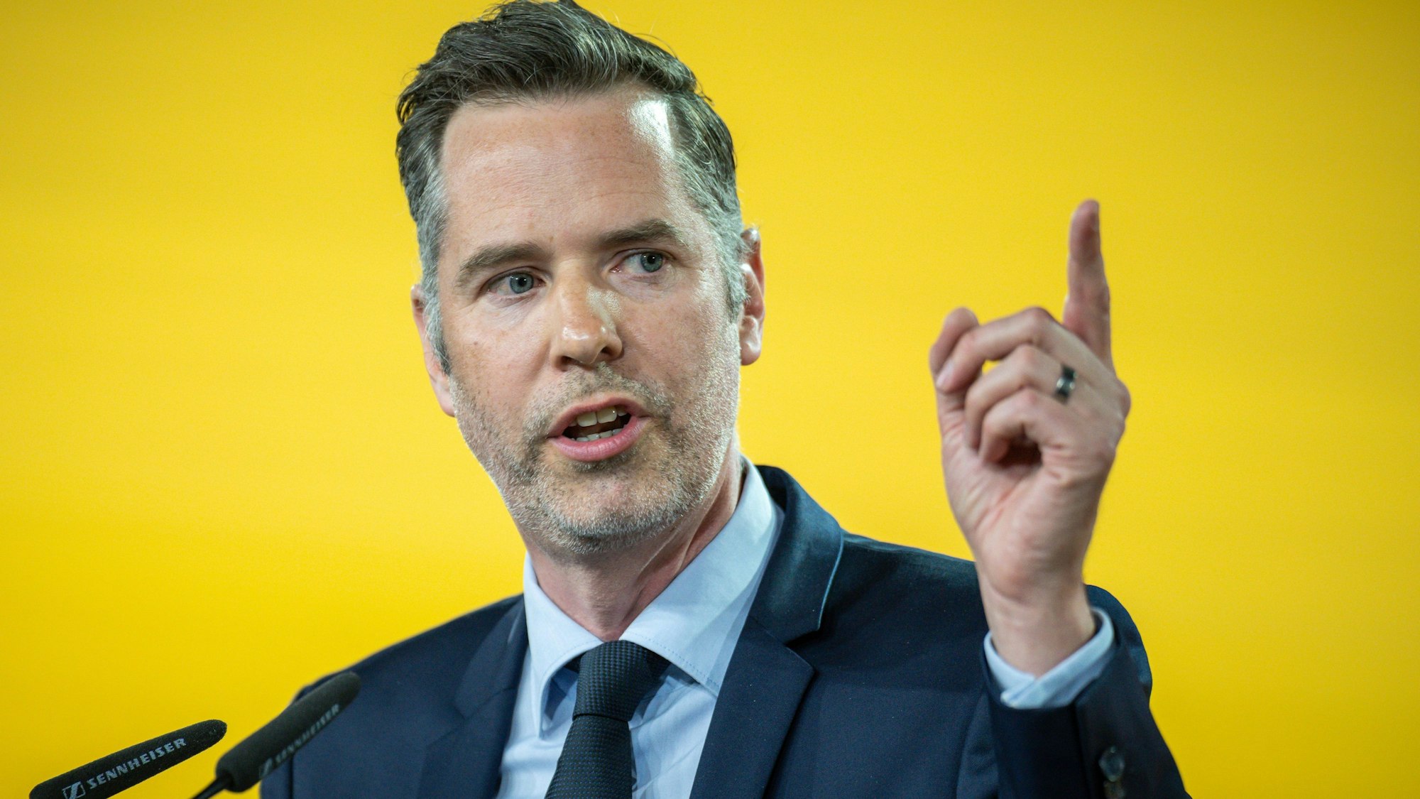 Es ist Christian Dürr mit erhobenem Finger vor einem gelben Hintergrund zu sehen.