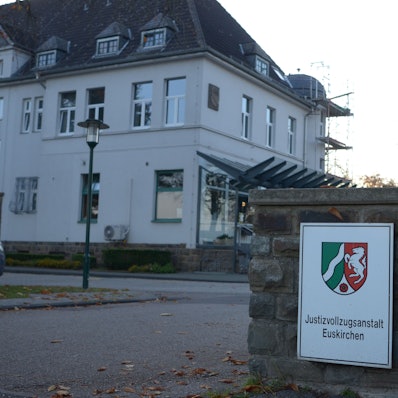 Am Eingang der Justizvollzugsanstalt Euskirchen hängt ein Schild mit dem Wappen des Landes NRW. Im Hintergrund sieht man ein Gebäude.