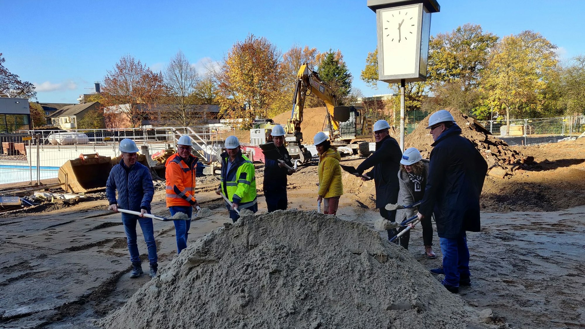 Vertreter der Stadt und der Bauunternehmen stechen auf der Baustelle im Freibad mit Schaufeln in einen Sandhaufen.