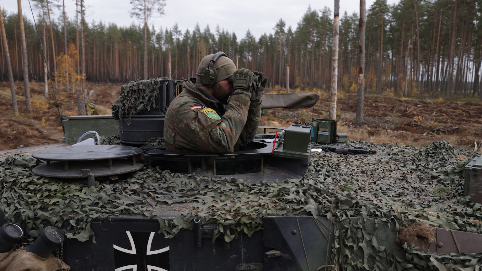 Ein Panzer-Kommandant der Bundeswehr guckt aus der Kommandantenkuppel eines Leopard-Panzers und blickt durch ein Fernglas.
