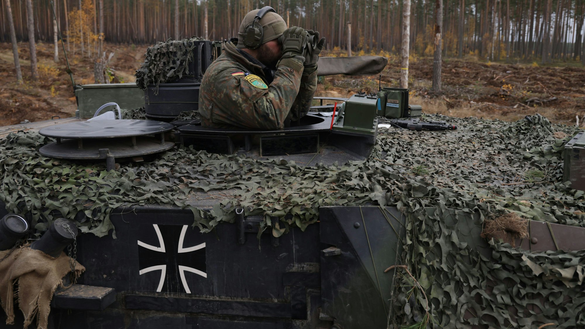 Ein Panzer-Kommandant der Bundeswehr guckt aus der Kommandantenkuppel eines Leopard-Panzers und blickt durch ein Fernglas.