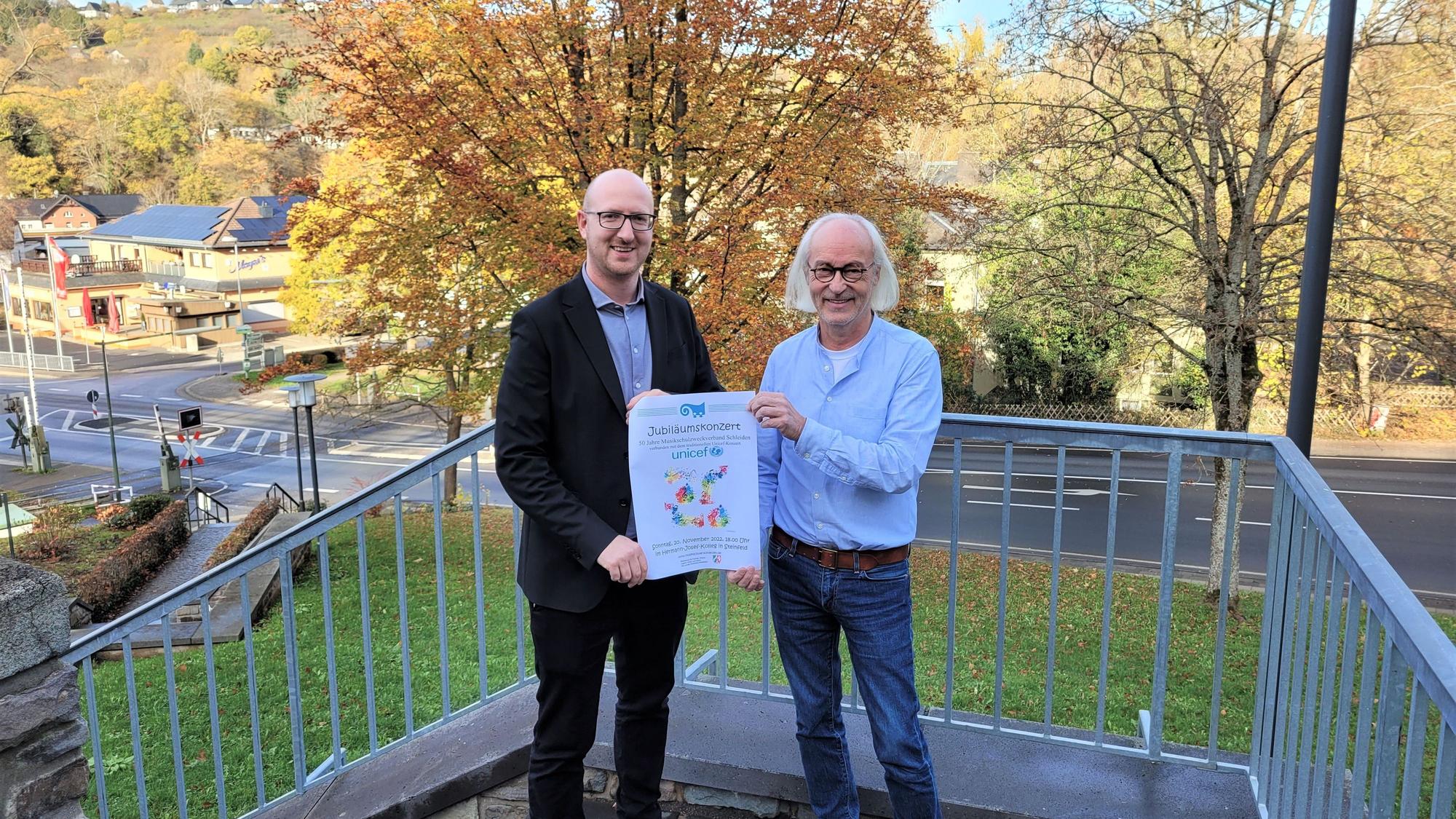 Bürgermeister Ingo Pfennings (l.) und Musikschulleiter Bernhard Vorhagen präsentieren auf einer Treppe das Plakat für das Festkonzert 50 Jahre Musikschulzweckverband Schleiden.