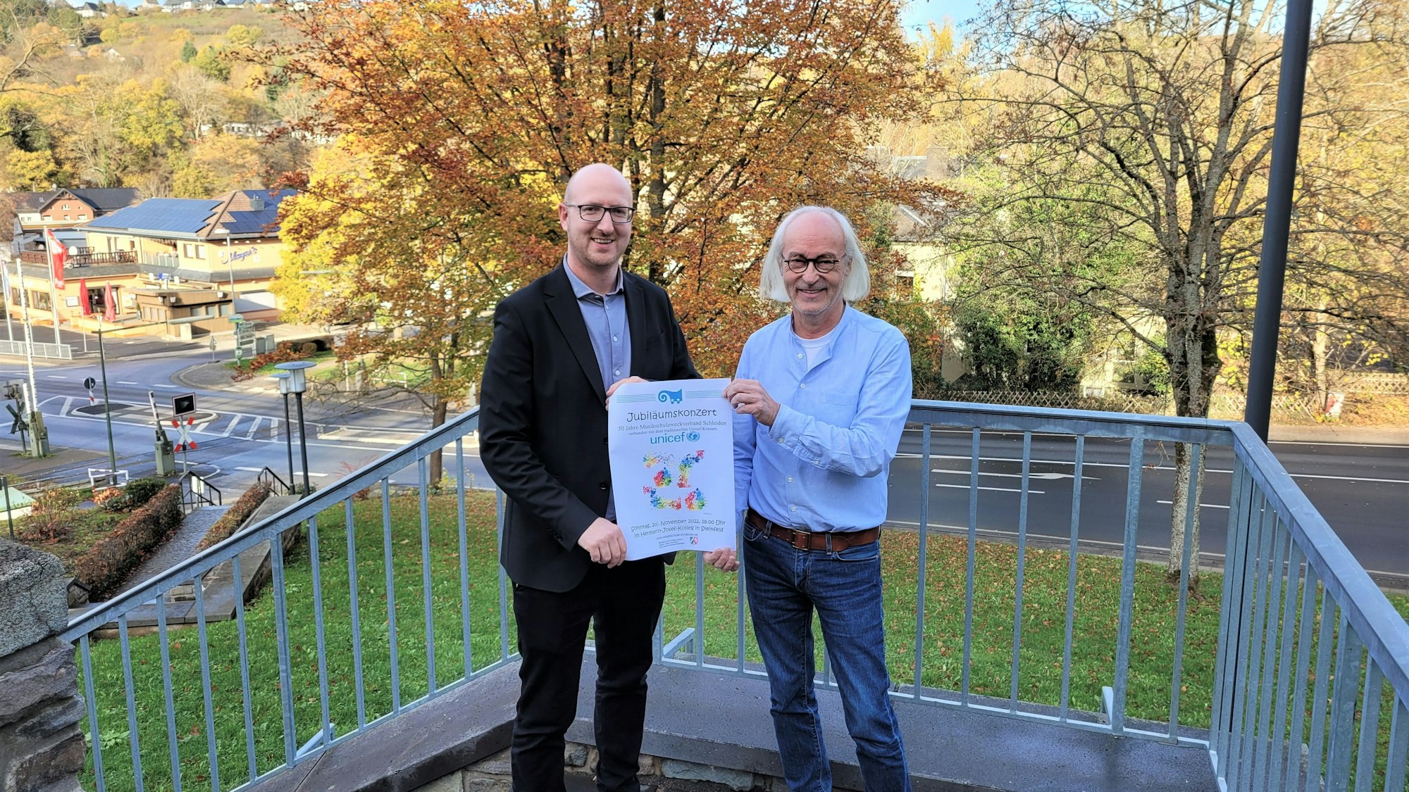 Bürgermeister Ingo Pfennings (l.) und Musikschulleiter Bernhard Vorhagen präsentieren auf einer Treppe das Plakat für das Festkonzert 50 Jahre Musikschulzweckverband Schleiden.