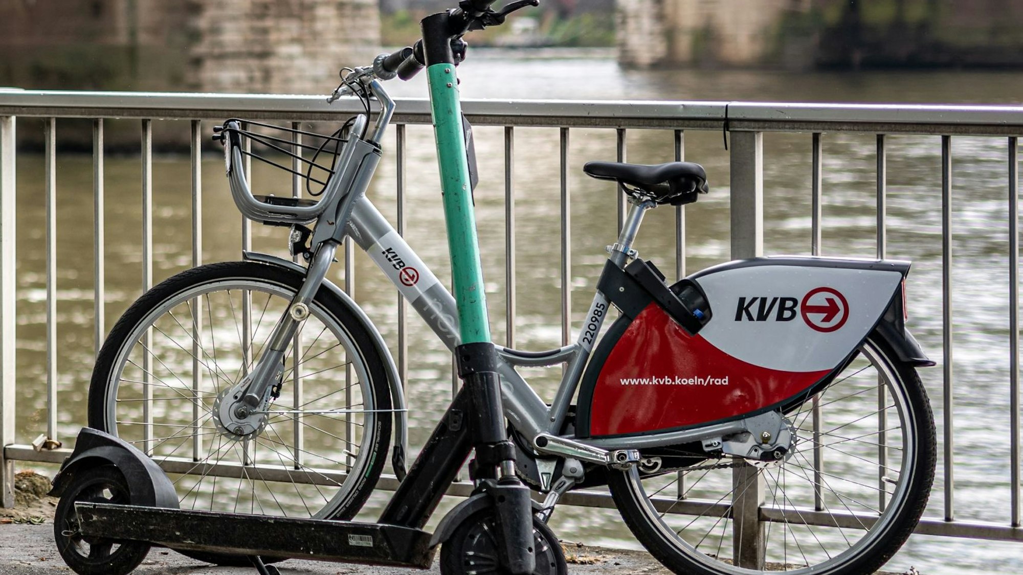 Ein E-Scooter und ein Leihfahrrad der Kölner Verkehrsbetriebe (KVB) stehen am Rheinufer vor der Hohenzollernbrücke in der Kölner Altstadt.