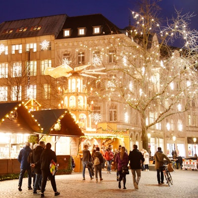 Der Weihnachtsmarkt auf dem Münsterplatz in 2021. Menschen laufen an Buden über einen hell erleuchteten Weihnachtsmarkt. (Symbolbild)