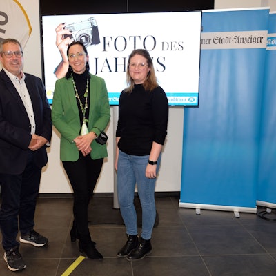 Ein Mann und zwei Frauen stehen vor einem Bildschirm mit der Aufschrift „Foto des Jahres“. Daneben stehen Banner vom „Kölner Stadt-Anzeiger“ und „Kölnische Rundschau“.