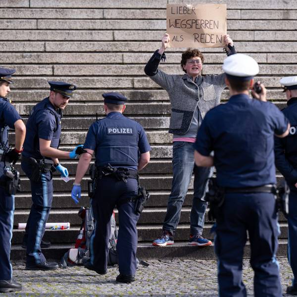 Ein Klimaaktivist steht vor der bayerischen Staatskanzlei und halten ein Schild mit der Aufschrift„ Lieber wegsperren als reden“ in den Händen. Um ihn herum stehen Polizisten.