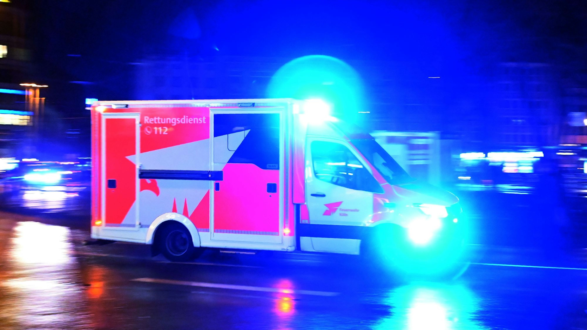 Ein Rettungswagen rast nachts mit Blaulicht über die Straße.