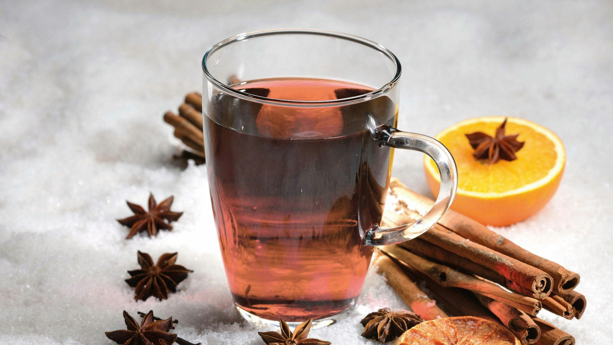 Nelken, Zimtstangen und Orangen liegen um einen Glühwein herum.