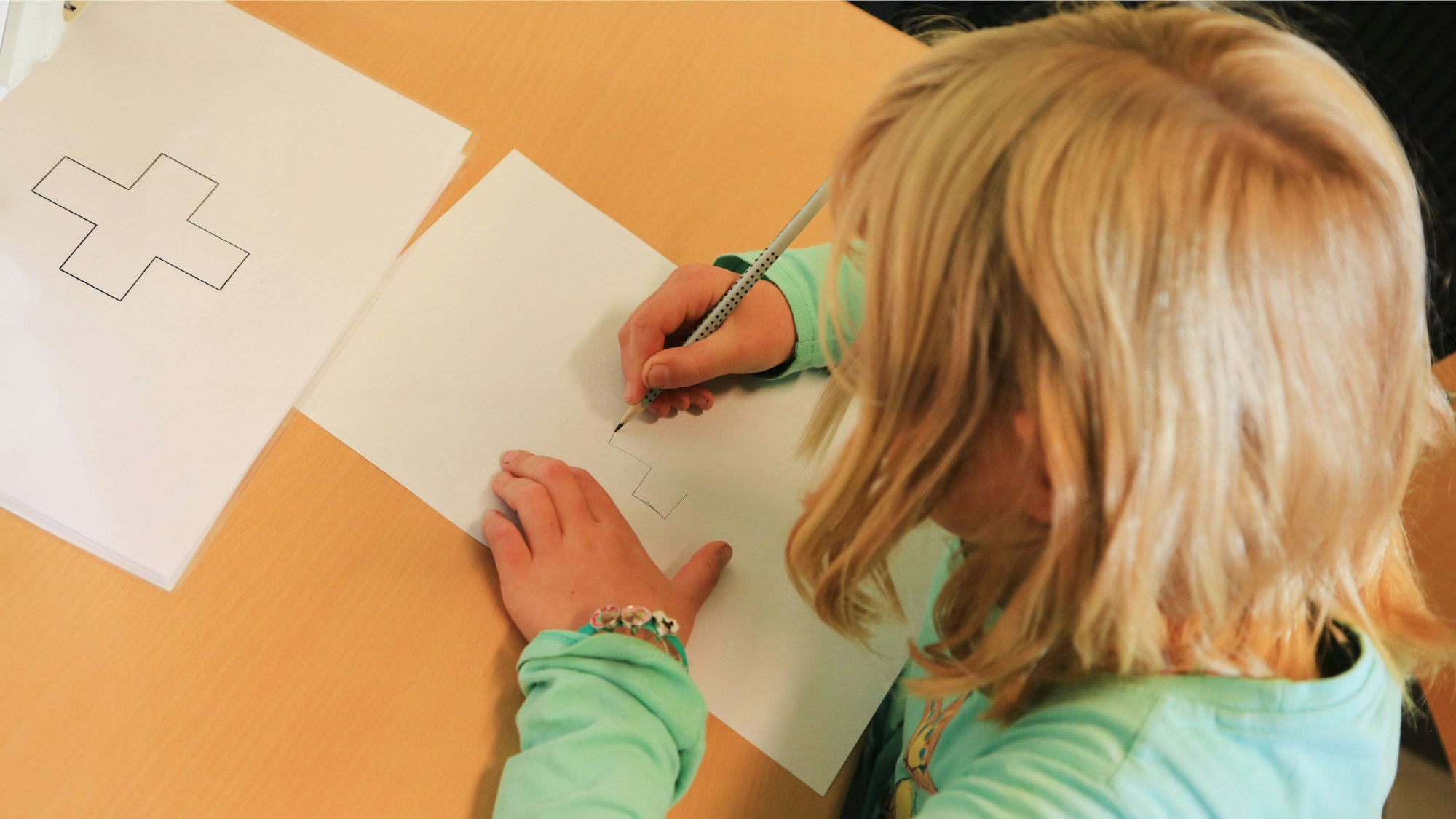 Ein Kind zeichnet ein auf einem Zettel abgebildetes Kreuz ab.