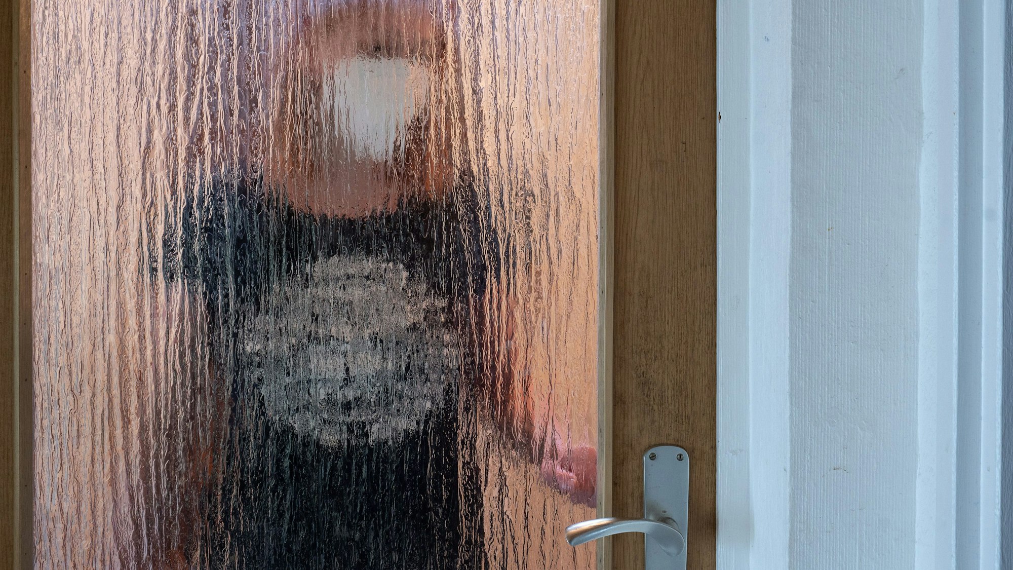 Eine Frau steht während der Isolation nach einem positiven PCR-Test hinter einer Glastür.