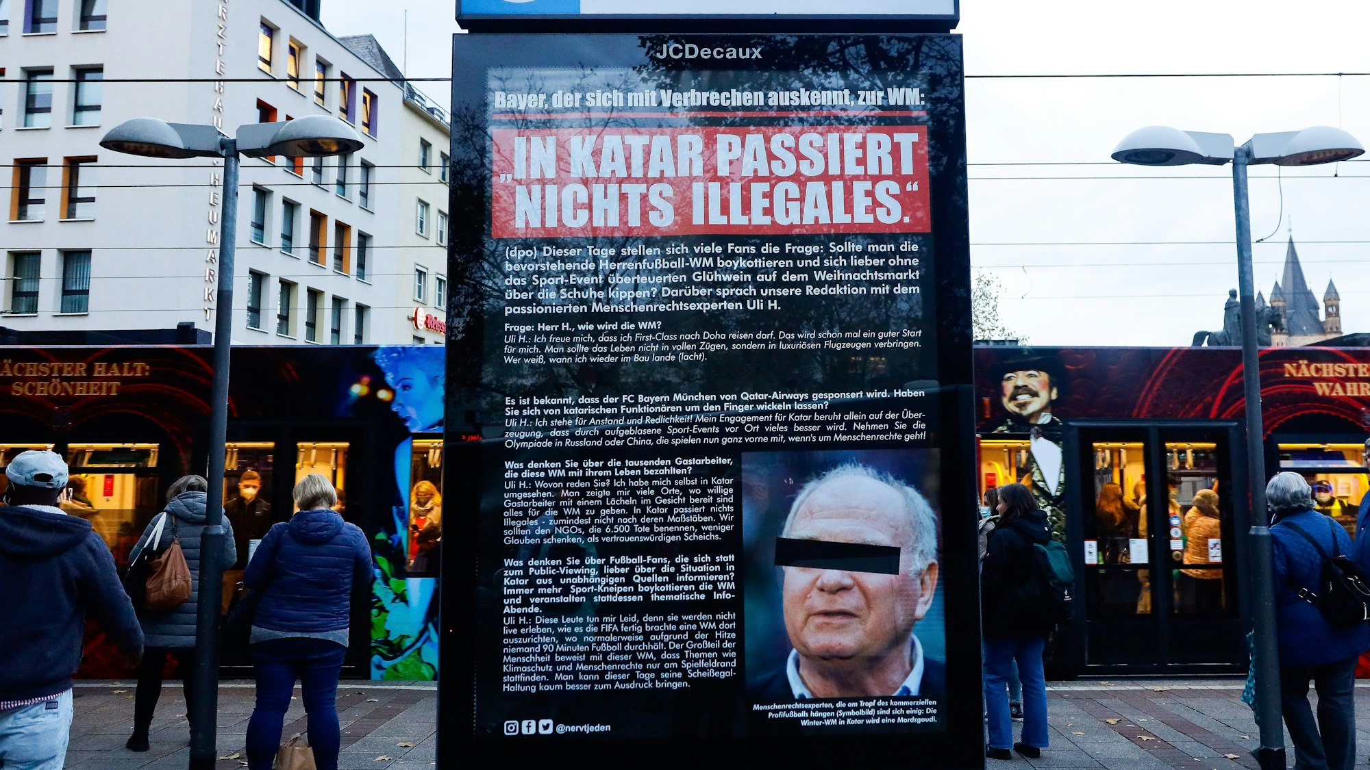 Ein Plakat, das wie ein Zeitungsartikel gestaltet ist, hängt in einem Schaukasten am Heumarkt unter dem Zeichen für die U-Bahn-Haltestelle. Darauf ist ein Foto von Uli Hoeneß mit einem schwarzen Balken vor den Augen zu sehen.