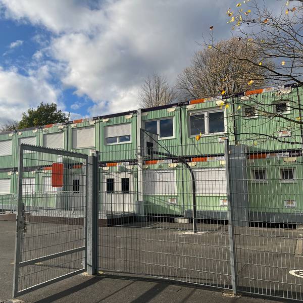 Grüne Container stehen auf einem kargen Schulhof.