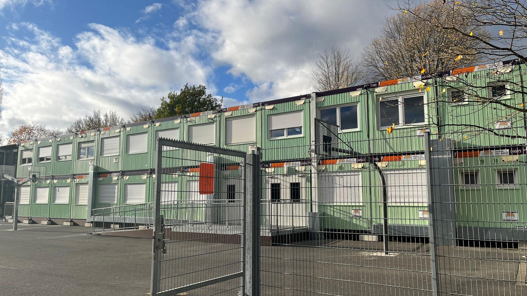 Mintgrüne Container stehen auf einem Schulhof.