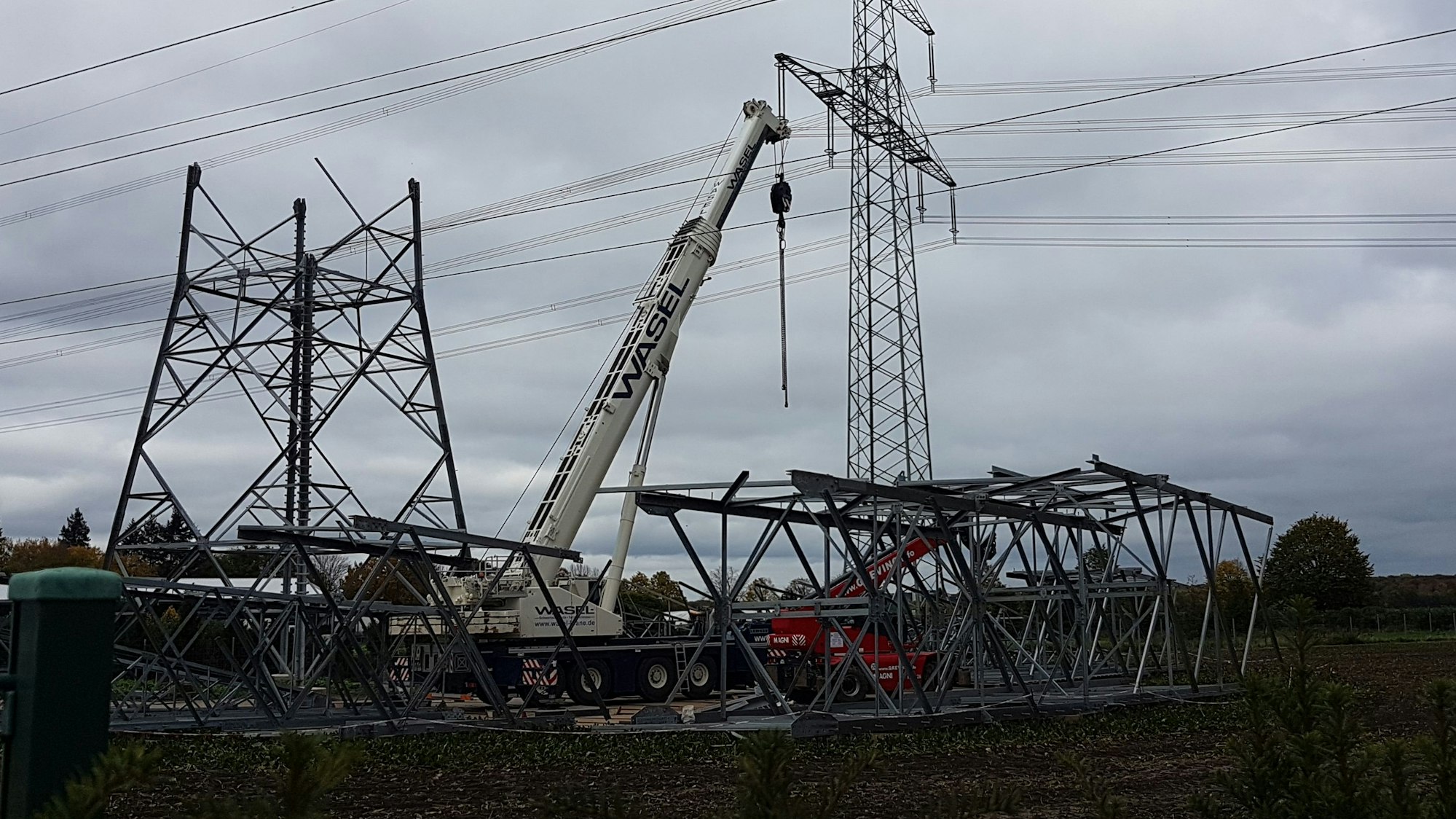 Auf einem Feld stehen zwei Strommasten, einer davon nur halb fertig, dahinter ein Bagger.