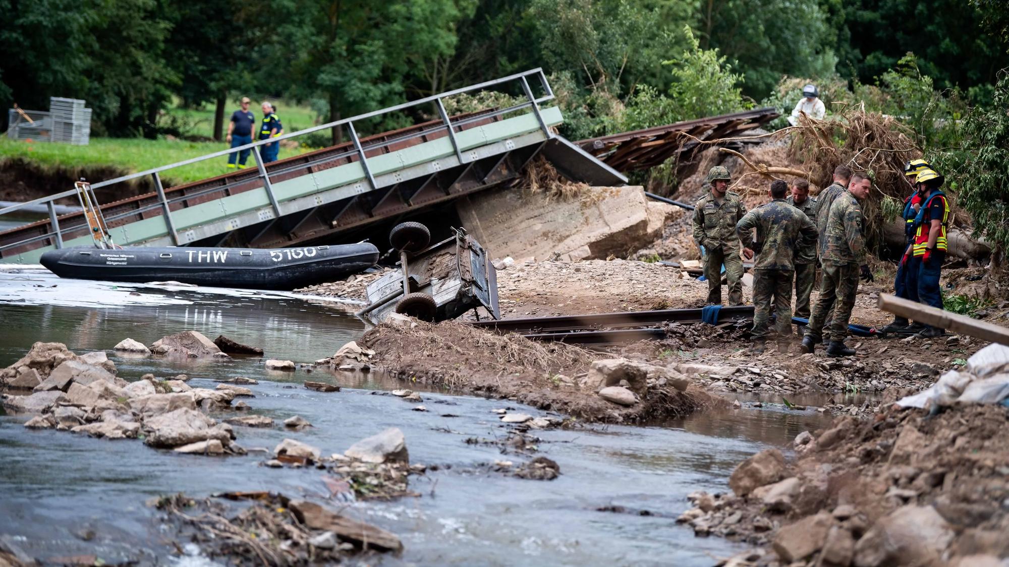 Die Brücke liegt schief in der Erft, viele Personen stehen am Ufer.