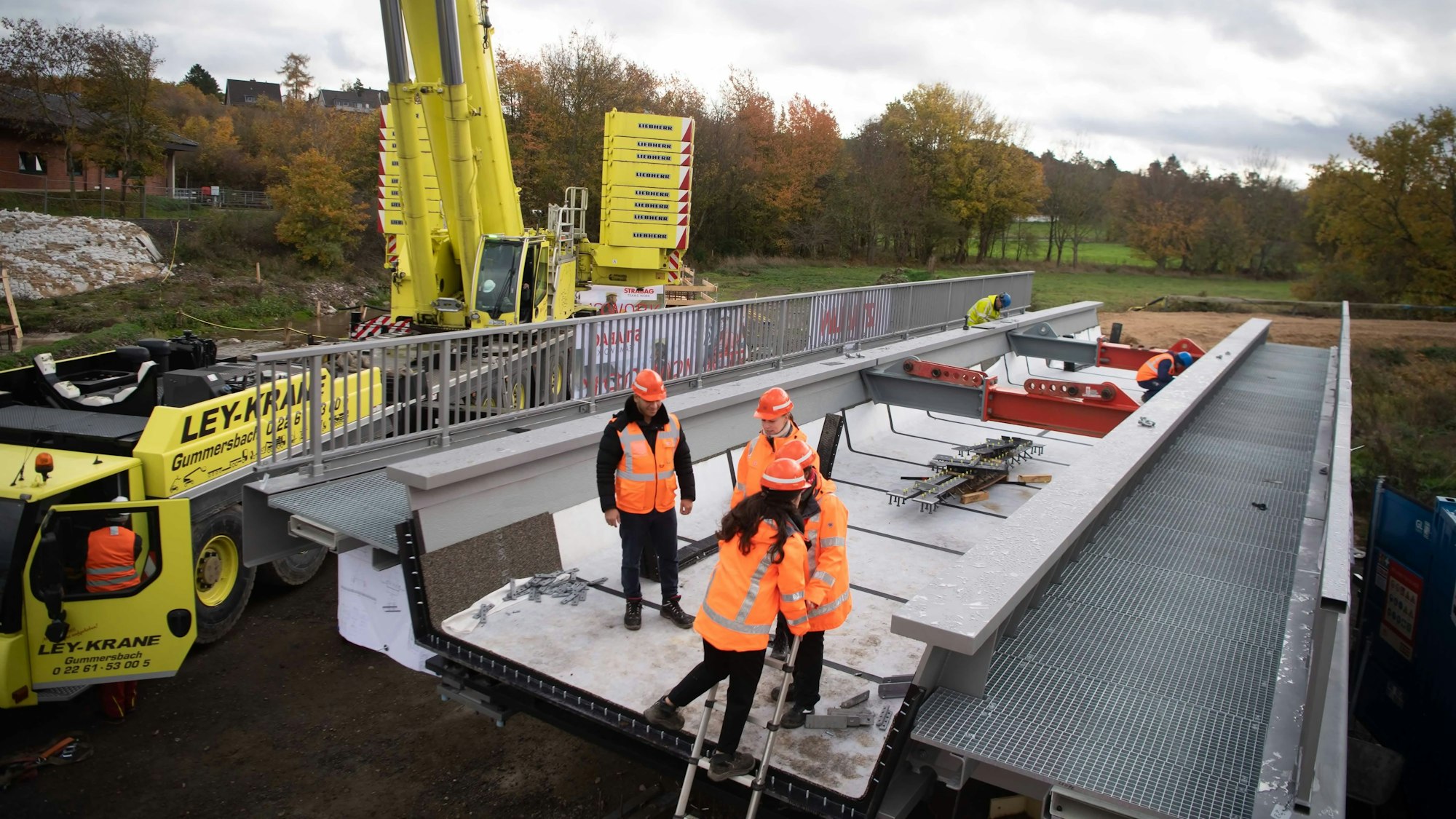 Vier Personen in orangen Jacken und Helmen stehen auf der Eisenbahnbrücke.