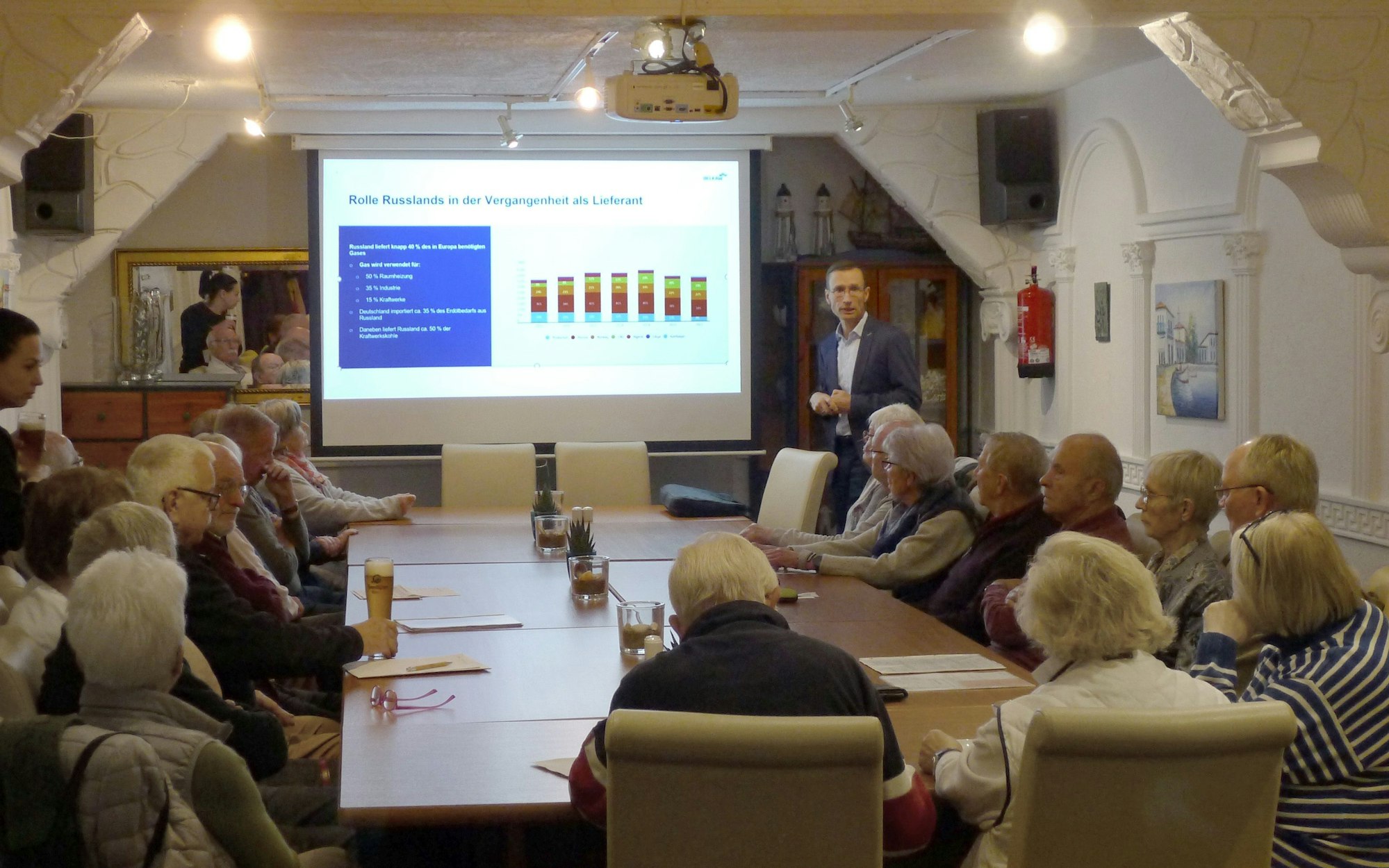 Senioren sitzen um einen Tisch und verfolgen einen Lichtbildvortrag von Referent Frank Burghardt.